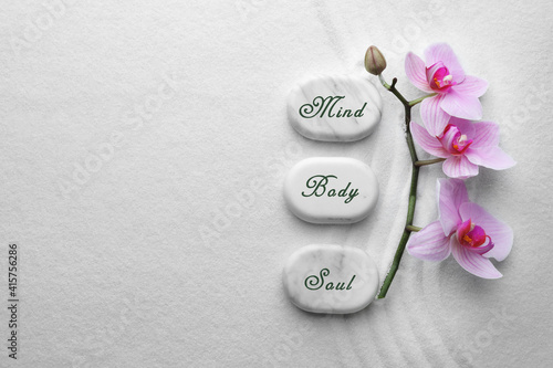 Canvas Print Stones with words Mind, Body, Soul and flowers on sand, flat lay