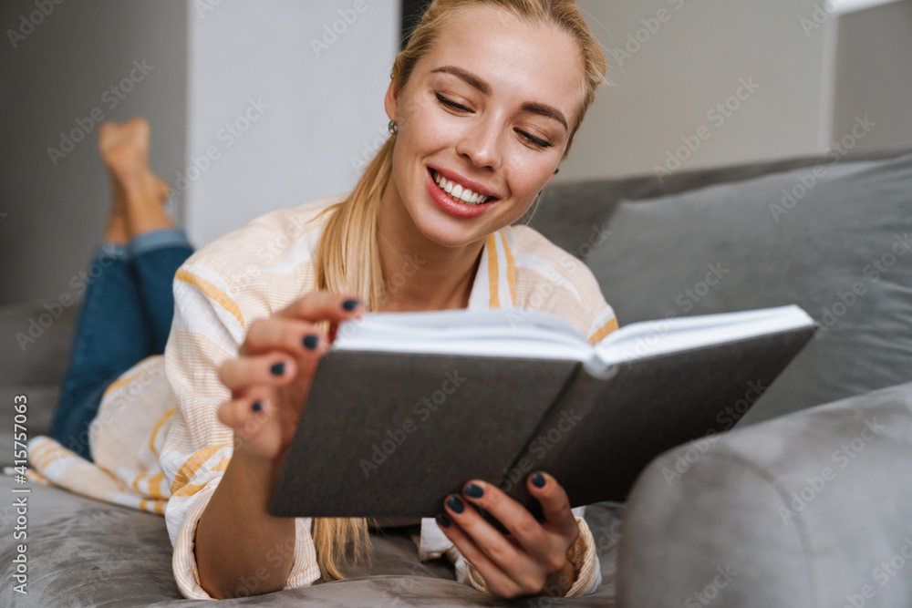 Happy woman smiling and reading book while lying on couch Happy woman smiling and reading book while lying on couch