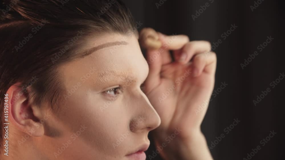 Drag artist - young man blending in the contour on his eyebrows and forehead Drag artist - young man blending in the contour on his eyebrows and forehead
