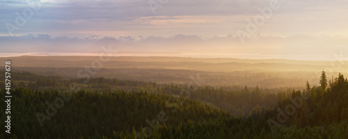 looking down onto misty forest valley at dawn with distant coast and mountains in background