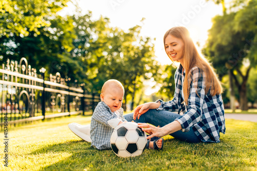 Little child with mom playing with soccer ball on the lawn in the park