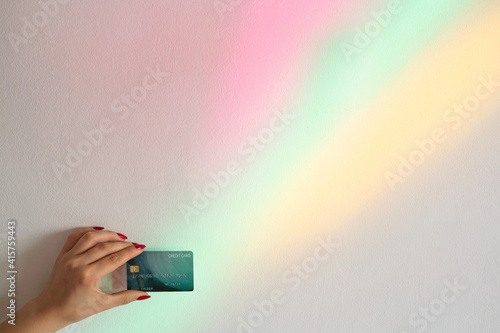 Bank payments. Online shopping. Personal offer. Financial operation. Female hand holding credit card on blur rainbow overlay glowing neon lights background.