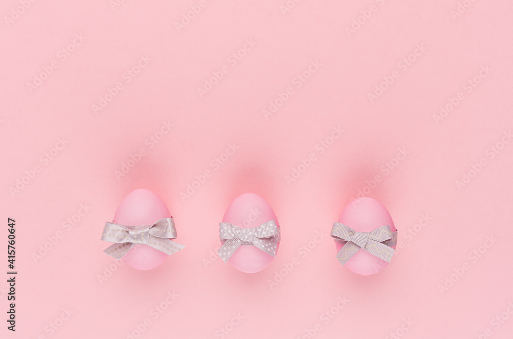 Sweet easter background with pink easter eggs with silver bow in row on pastel pink color.