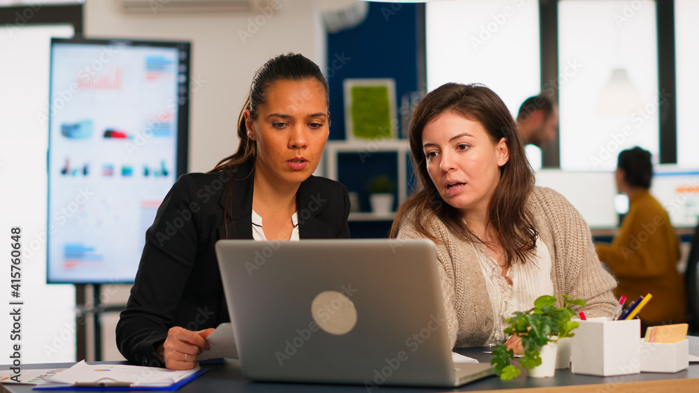 Young project manager and company director talking about business strategy in front of laptop computer in creative office. Diverse team of coworkers working in busy marketing agency workplace. Young project manager and company director talking about business strategy in front of laptop computer in creative office. Diverse team of coworkers working in busy marketing agency workplace.