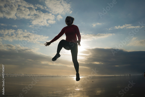 silhouette of happy and excited woman jumping on the air above sea water at beautiful beach on sunset in freedom and excitement concept