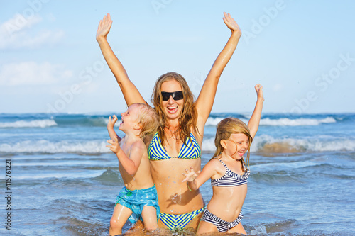 Happy family have fun on tropical sea beach resort. Funny young mother with children swim in water pool, raise up the hands. Active lifestyle, people travel activity on summer holiday with kids.