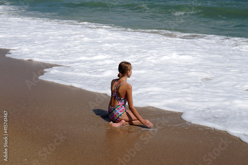 teenage girl sitting alone on the wet sand and looking at the sea