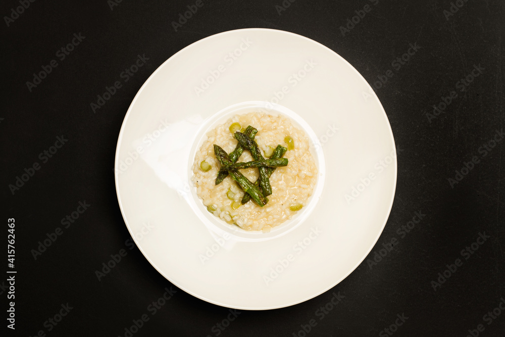 Delicioso risotto con espárragos dentro de un plato blanco redondo sobre un fondo negro. Vista superior. Copy sace Delicioso risotto con espárragos dentro de un plato blanco redondo sobre un fondo negro. Vista superior. Copy sace