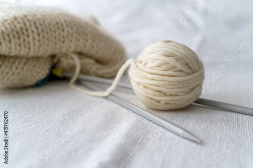 Grey knitting needles with knitting made thick wool yarn on white background with soft focus. Female hobby and leisure knitting concept.