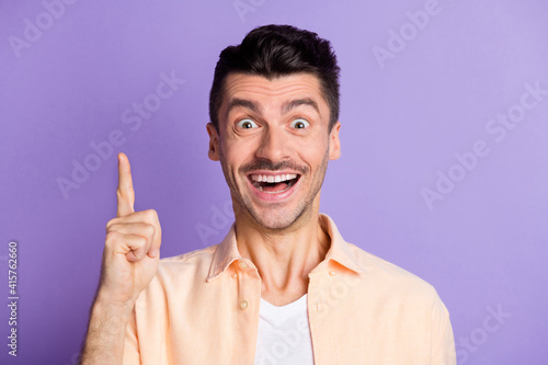 Portrait of funny brunet hair guy point up wear peach shirt isolated on lilac color background