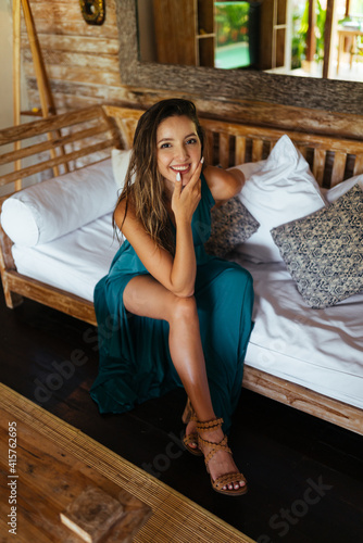 leaning her elbow on her knee and putting her chin on the palm of a girl in a long dress sitting on the edge of the bed among the pillows. High quality photo