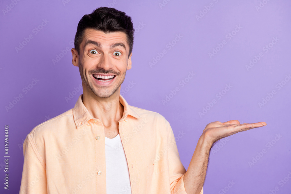 Photo of positive man hand demonstrate empty space wear beige shirt isolated violet color background Photo of positive man hand demonstrate empty space wear beige shirt isolated violet color background