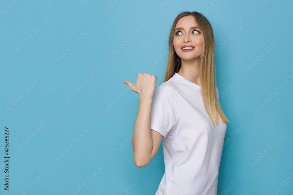 Smiling Young Woman Points With Thumb Behind Herself. Smiling Young Woman Points With Thumb Behind Herself.