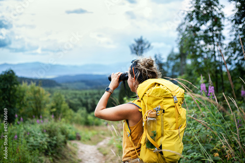Rear view of woman hiker with backpack on a hiking trip in nature, using binoculars. photo