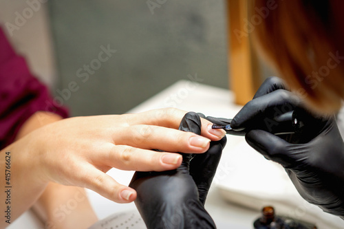 Close up of manicure master covering nails with the transparent polish of female nails in a nail salon