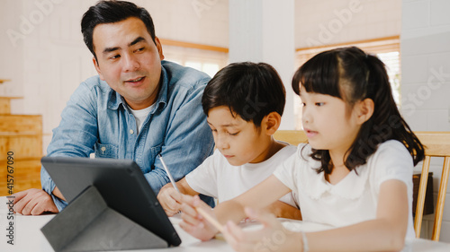 Happy Asia family homeschooling, father teach children using digital tablet in living room at home. Spending time together, Self-isolation, Social distancing, Quarantine for corona virus prevention. © tirachard
