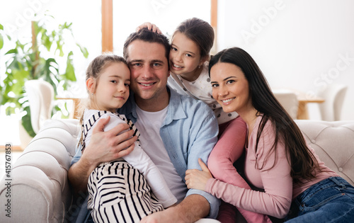 Parents with small daughters sitting on sofa indoors at home, looking at camera.