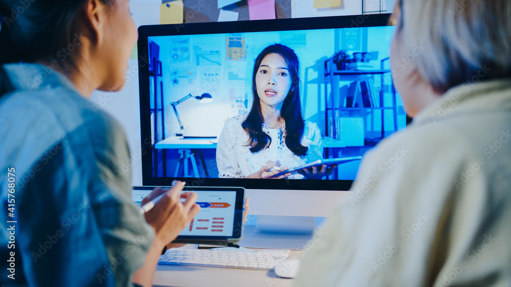 Asia businesswomen using desktop talk to colleagues about plan in video call meeting at living room. Working from house overload at night, remotely work, social distancing, quarantine for coronavirus.
