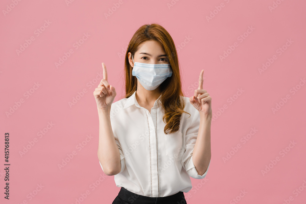 Young Asia girl wearing medical face mask shows something at blank space with dressed in casual cloth and looking at camera isolated on pink background. Social distancing, quarantine for corona virus. Young Asia girl wearing medical face mask shows something at blank space with dressed in casual cloth and looking at camera isolated on pink background. Social distancing, quarantine for corona virus.