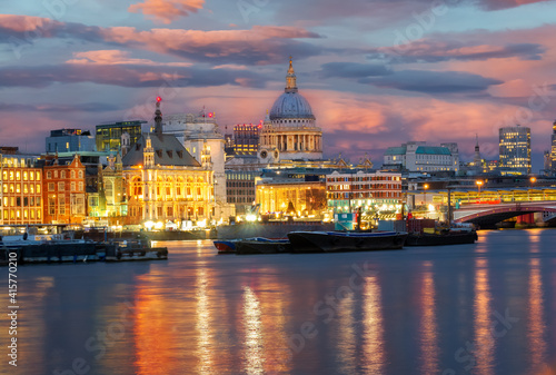 Cityscape of London at dusk, view of the famous Saint Pauls Cathedral ans boats on the River Thames illuminated at sunset.