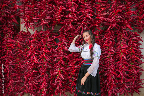 Young woman dressed on traditional Serbian Balkan clothing, national folk costume.Posing near of lot red paprika peppers