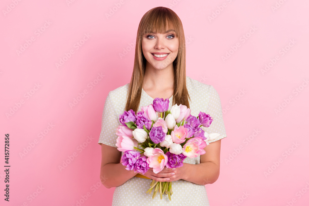 Portrait of pretty cheerful girl holding in hands flowers congrats isolated over pink pastel color background