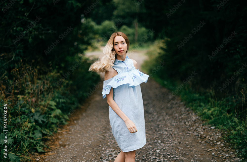 Young attractive elegant blonde girl in blue romantic dress posing on the road in the countryside Young attractive elegant blonde girl in blue romantic dress posing on the road in the countryside