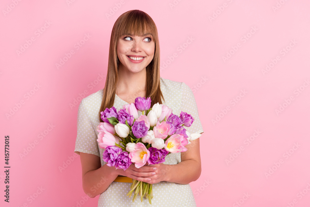 Portrait of attractive cheerful curious girl holding in hands flowers thinking copy space isolated over pink pastel color background