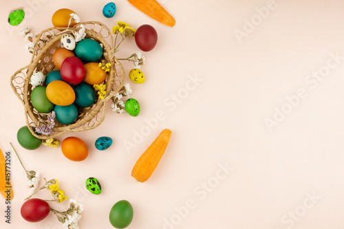 wooden wicker basket with colored colorful eggs on a pastel beige background top view