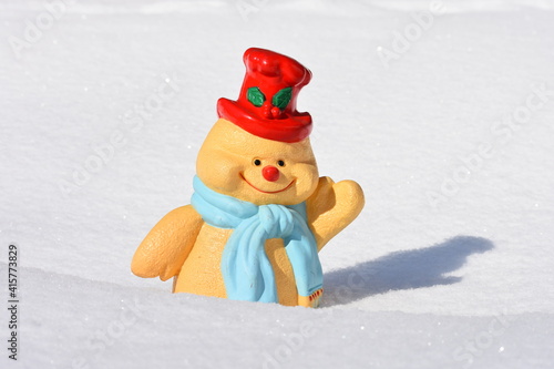 Decorative small plastic cheerful snownman with red hat standing in fresh snow on a sunny day 