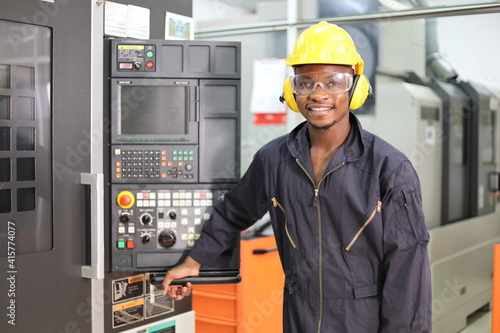 Portrait of African American mechanic engineer worker wearing safety equipment beside the automatic lathe machine in manufacturing factory