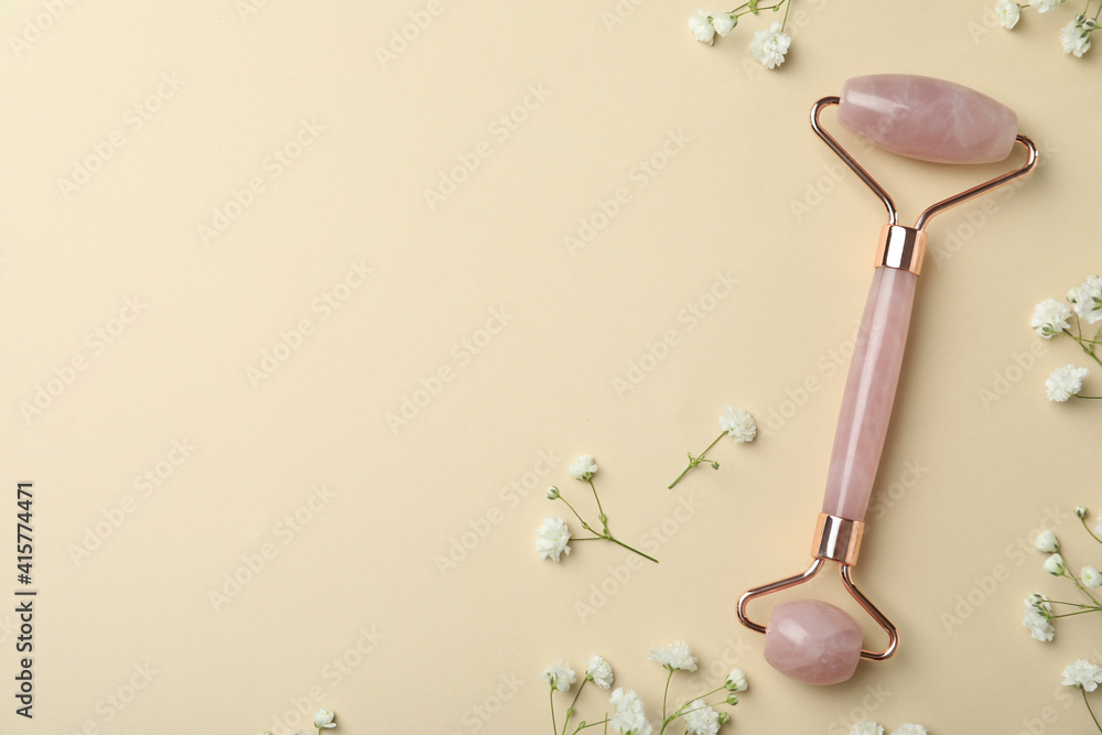 Natural face roller and flowers on beige background, flat lay. Space for text Natural face roller and flowers on beige background, flat lay. Space for text