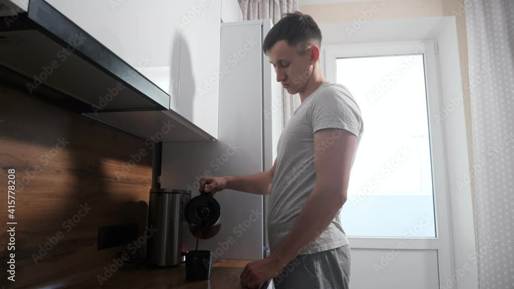Sleepy man pours coffee from the coffee maker and accidentally spills it on the table. Sleepy man pours coffee from the coffee maker and accidentally spills it on the table.