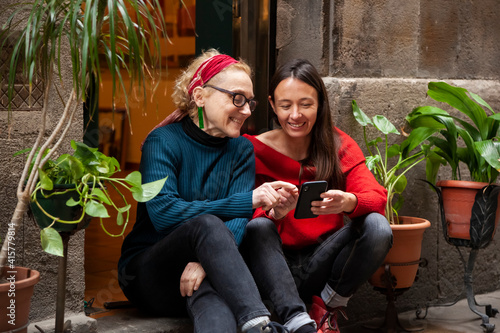 Candid portrait of two female friends chatting, laughing and using a smart phone