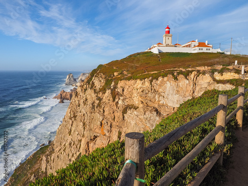 Cabo da Roca lighthouse on the hill in the blue sky background, overlooking the Atlantic Ocean. Panoramic viewpoint, cape of the Sintra Mountain Range and the westernmost point of European continent. photo