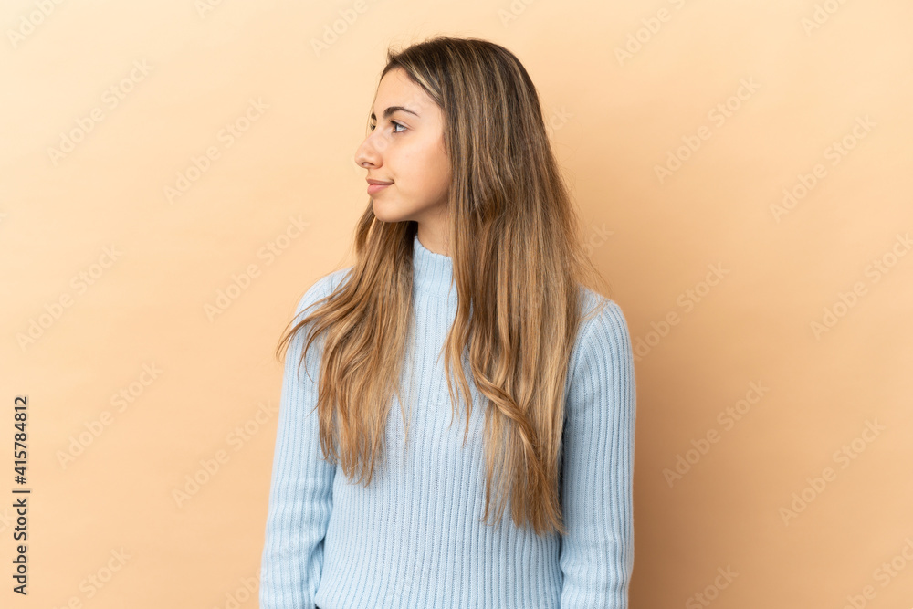 Obraz premium Young caucasian woman isolated on beige background looking to the side
