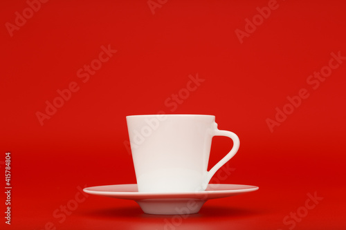 White porcelain coffee cup on saucer against red background with copy space. Minimalistic still life with coffee against red background. Concept of energy drinks