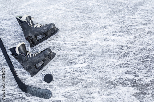 Old scratched black hockey male skates, stick and rubber puck on ice background. Closeup. Empty place for text. Top down view. photo