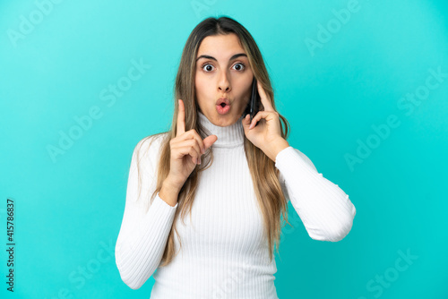 Young caucasian woman using mobile phone isolated on blue background intending to realizes the solution while lifting a finger up