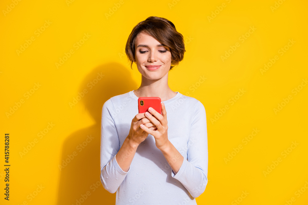 Photo portrait of woman texting holding phone in two hands isolated on bright yellow colored background