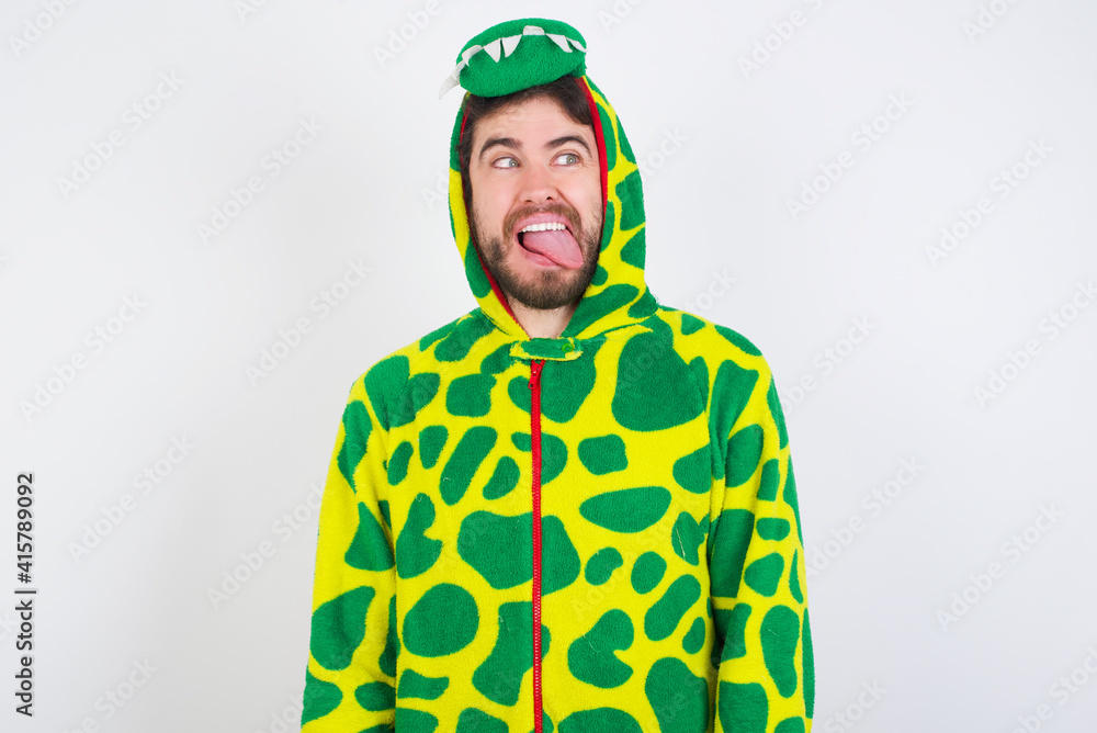 Fototapeta premium young caucasian man wearing a pyjama standing against white wall showing grimace face crossing eyes and showing tongue. Being funny and crazy