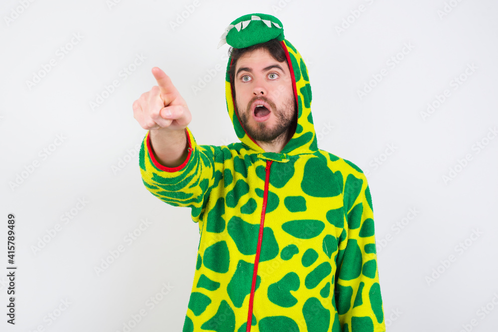 Fototapeta premium young caucasian man wearing a pajama standing against white wall Pointing with finger surprised ahead, open mouth amazed expression, something on the front.