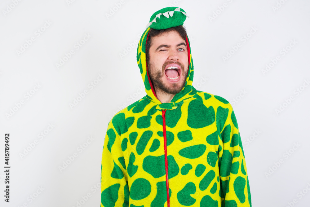 Fototapeta premium young caucasian man wearing a pajama standing against white wall winking looking at the camera with sexy expression, cheerful and happy face.