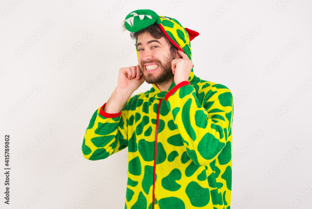 Fototapeta premium young caucasian man wearing a pajama standing against white wall covering ears with fingers with annoyed expression for the noise of loud music. Deaf concept.
