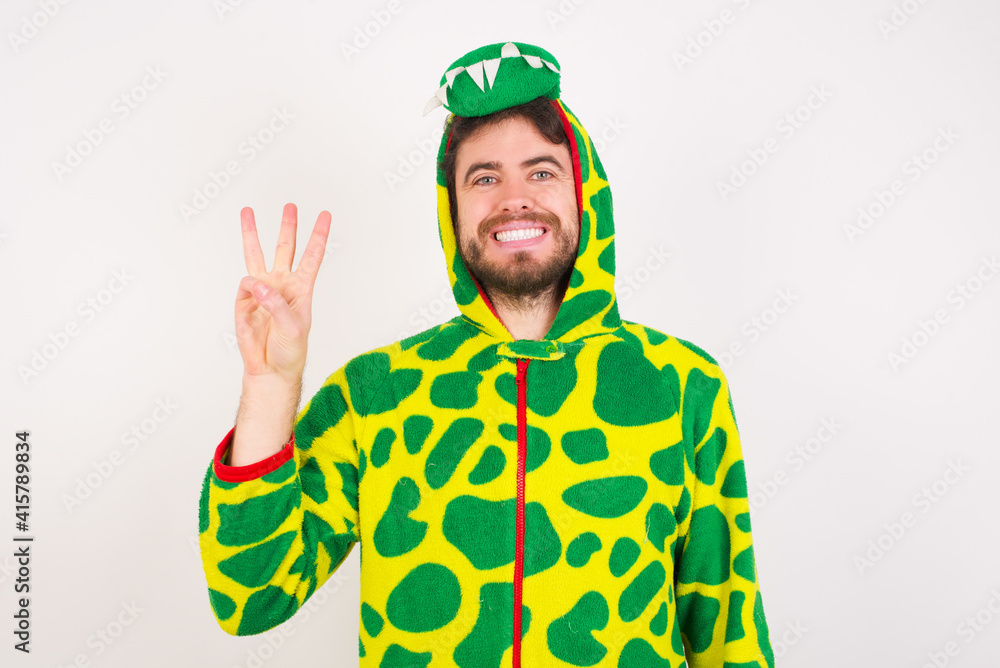 Fototapeta premium young caucasian man wearing a pajama standing against white wall showing and pointing up with fingers number three while smiling confident and happy.