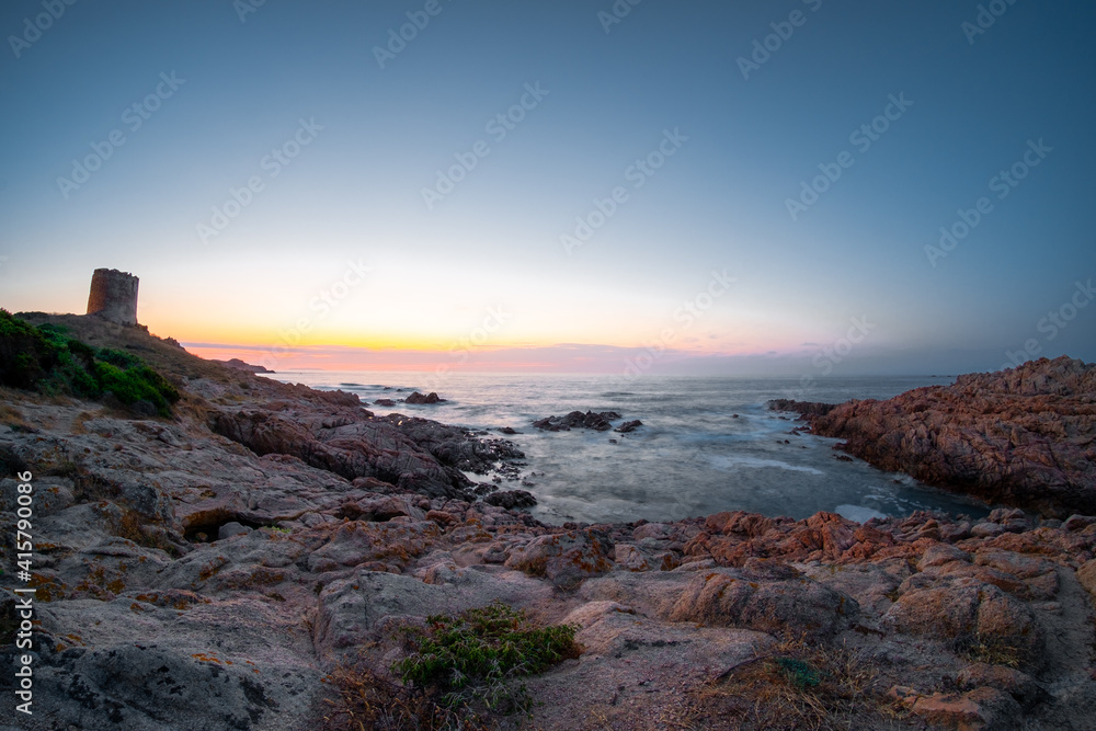 Coastal landscape in twilight time. Panoramic view on water eroded red rocks. Colourful sky after sunset.
