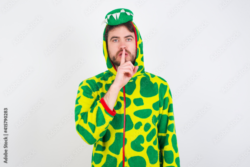 Fototapeta premium young caucasian man wearing a pajama standing against white wall makes silence gesture, keeps finger over lips. Silence and secret concept.