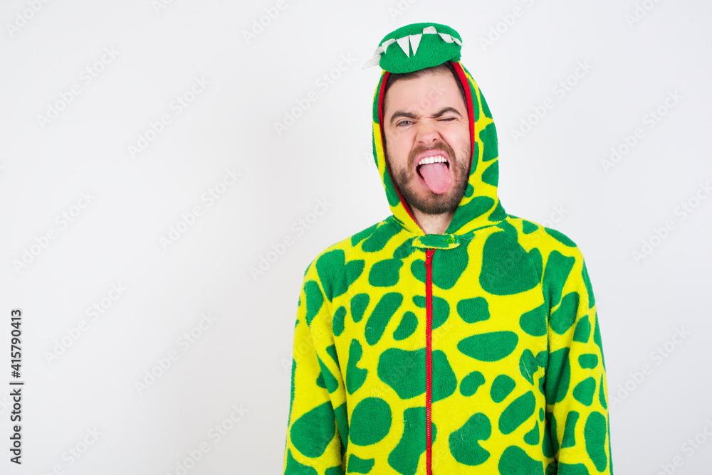 Fototapeta premium young caucasian man wearing a pajama standing against white wall sticking tongue out happy with funny expression. Emotion concept.