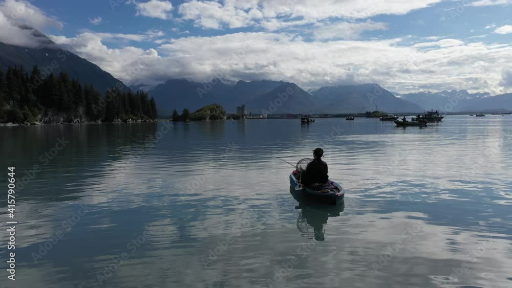 slow pan following Fisherwoman in kayak reeling in her rod and casting in harbor not far off a forest shoreline and surrounded by distant mountains on a sunny summer day. slow pan following Fisherwoman in kayak reeling in her rod and casting in harbor not far off a forest shoreline and surrounded by distant mountains on a sunny summer day.