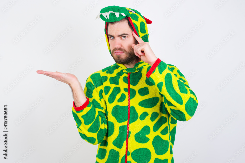 Fototapeta premium young caucasian man wearing a pajama standing against white wall confused and annoyed with open palm showing copy space and pointing finger to forehead. Think about it.